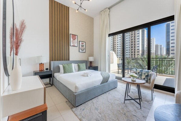 Een moderne hotelkamer met een groot bed, een kleintje tafeltje, een balkon met uitzicht op de stad en een groot raam.