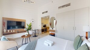 A modern hotel room with a large bed, a TV, a dining area, and a separate kitchen. - Serene Studio in the Heart of Town Square l Cycling Track (Town Square)
