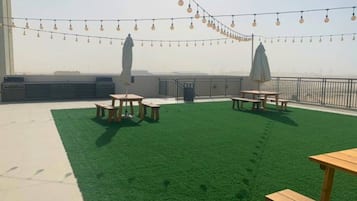 A rooftop terrace with artificial grass, picnic tables, and string lights.
