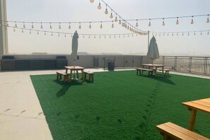 Une terrasse sur le toit, avec un revêtement d’herbe artificielle, des tables de pique-nique et des guirlandes lumineuses.