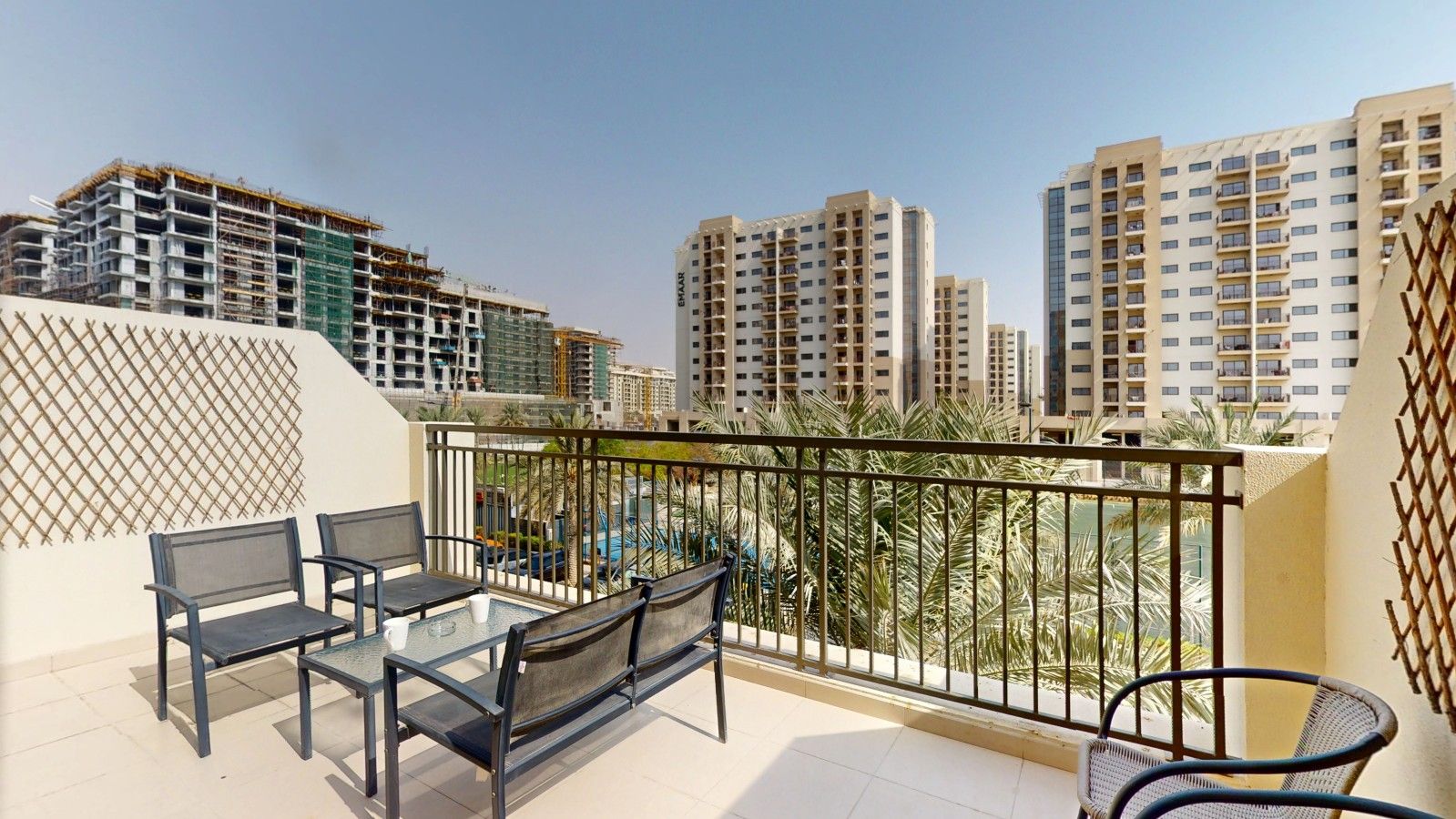 A balcony with a table and chairs, overlooking a cityscape with high-rise buildings.