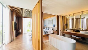 Una habitación de hotel moderna con una cama grande, un baño separado con bañera y una zona de estar con televisor.