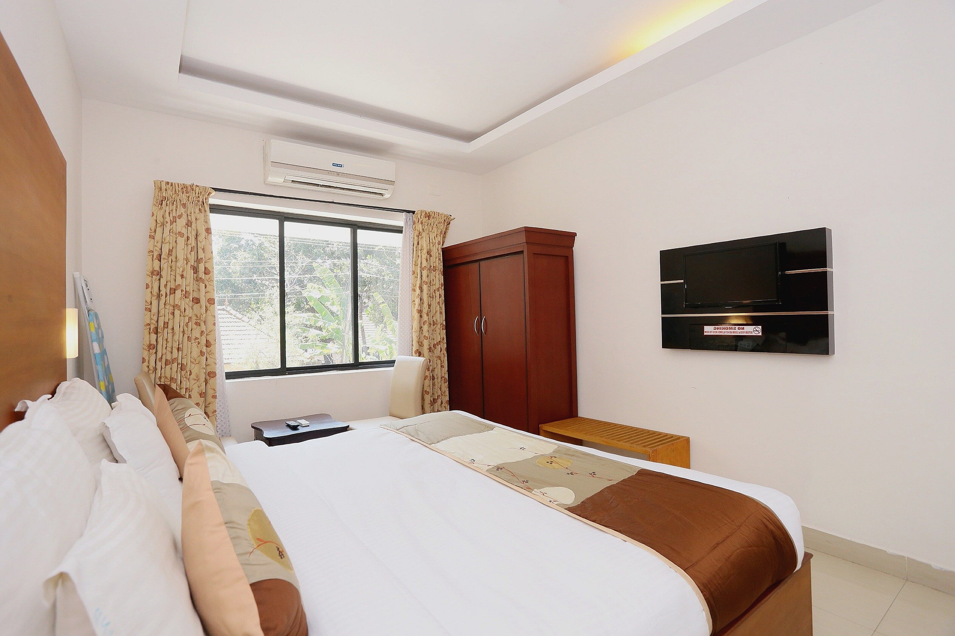 Una habitación de hotel con cama, armario, televisor y ventana con cortinas.