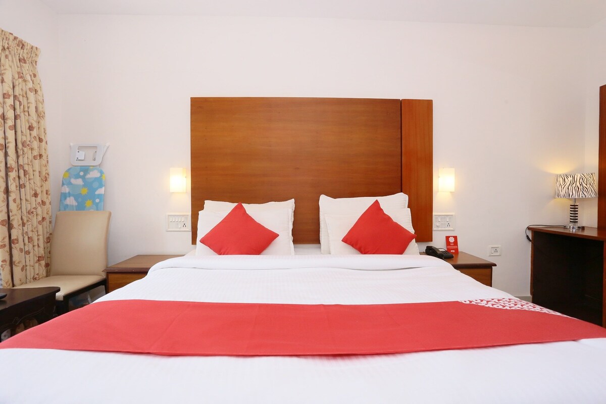 Habitación de hotel con una cama grande, dos mesitas de noche, una silla, una lámpara y un teléfono instalado en la pared.