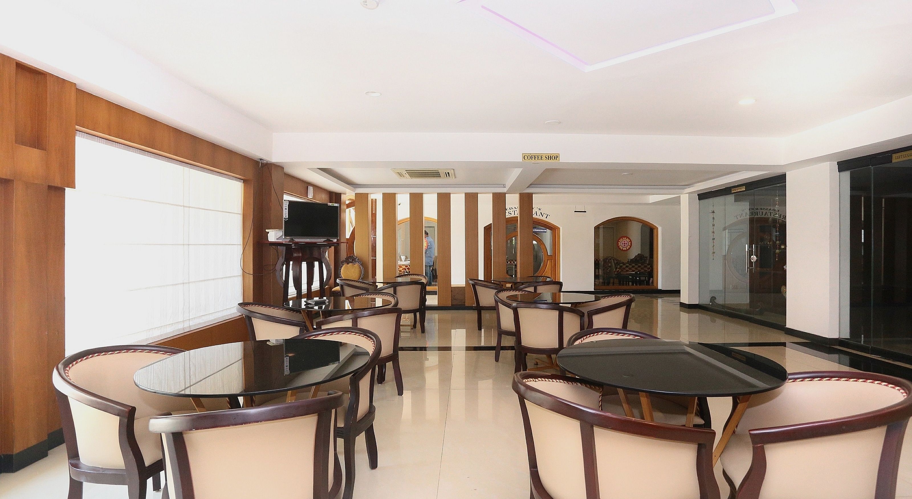 Un salón de conferencias con mesas y sillas redondas, un televisor sobre un pedestal, y un letrero de cafetería.