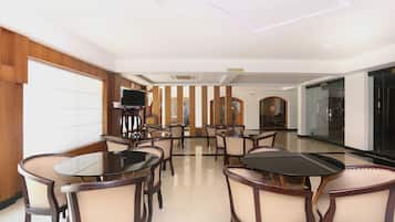 Un salón de conferencias con mesas y sillas redondas, un televisor sobre un pedestal, y un letrero de cafetería.