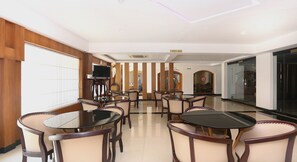 Un salón de conferencias con mesas y sillas redondas, un televisor sobre un pedestal, y un letrero de cafetería.