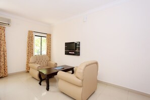 Una sala de estar con dos sillones color beige, una mesa de centro de madera y un televisor de pantalla plana montado en la pared.