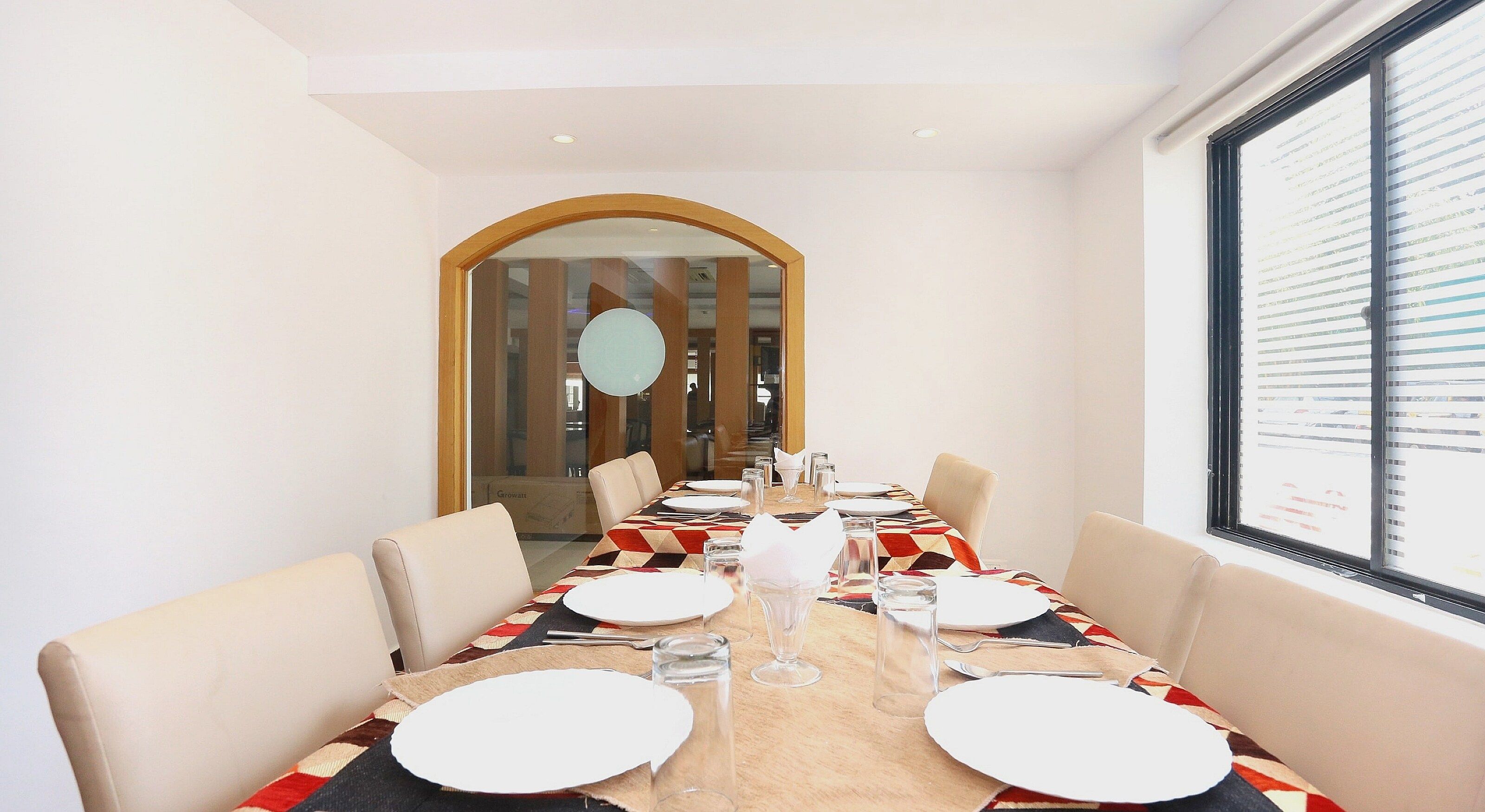 Een eetruimte met een lange tafel, gedekt voor vier personen, met een tafelkleed met een geometrisch patroon, witte borden en glazen.