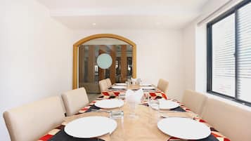 Een eetruimte met een lange tafel, gedekt voor vier personen, met een tafelkleed met een geometrisch patroon, witte borden en glazen.
