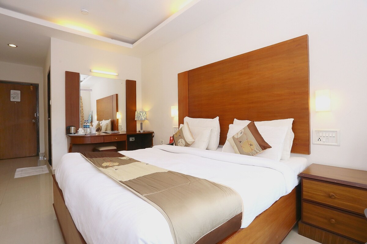 Una habitación de hotel con una cama grande, un cabecero de madera, una mesita de noche, un espejo y un tocador.