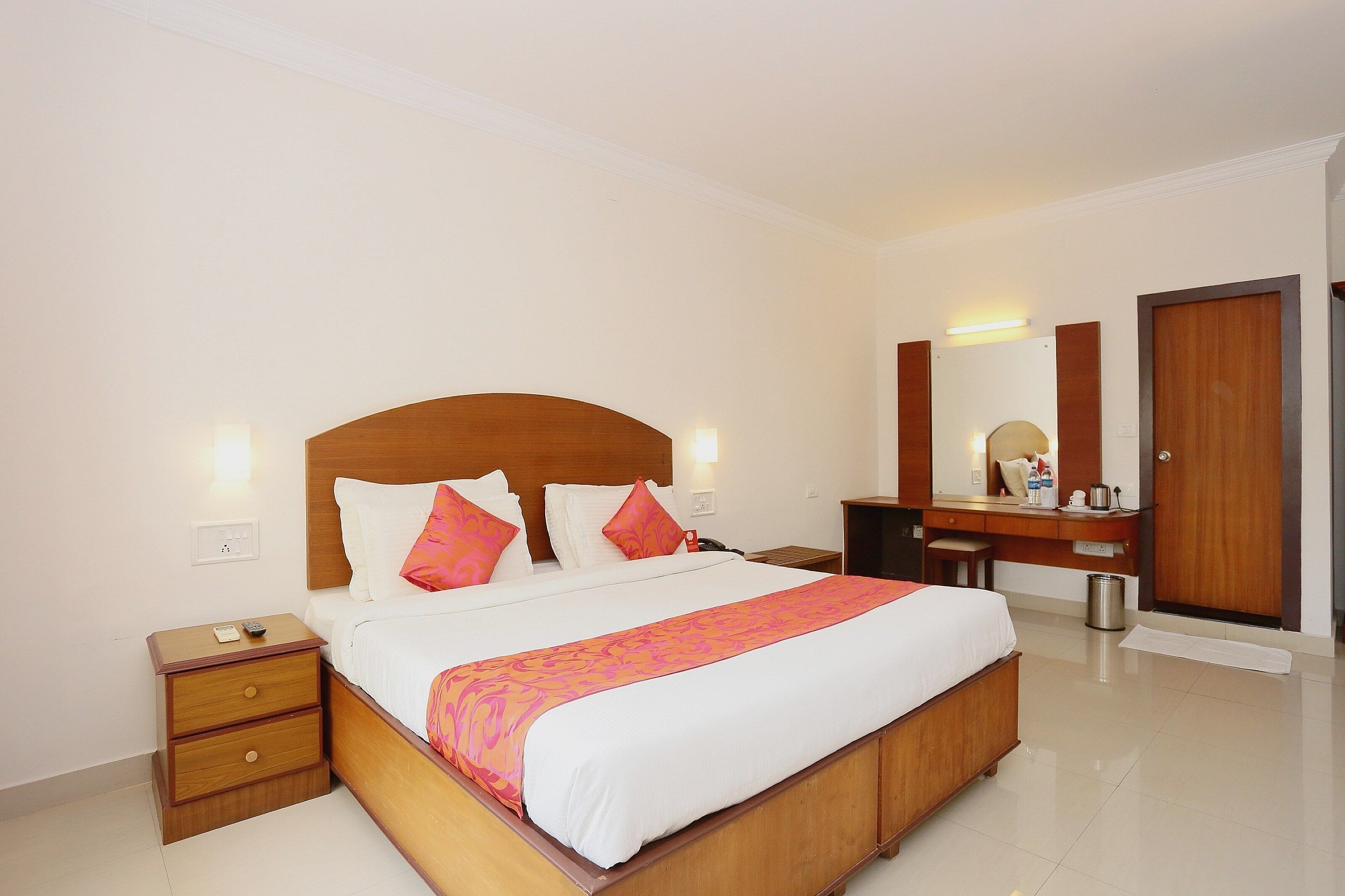 Una habitación de hotel con una cama grande, un cabecero de madera, una mesita de noche, un escritorio, un espejo y una puerta.