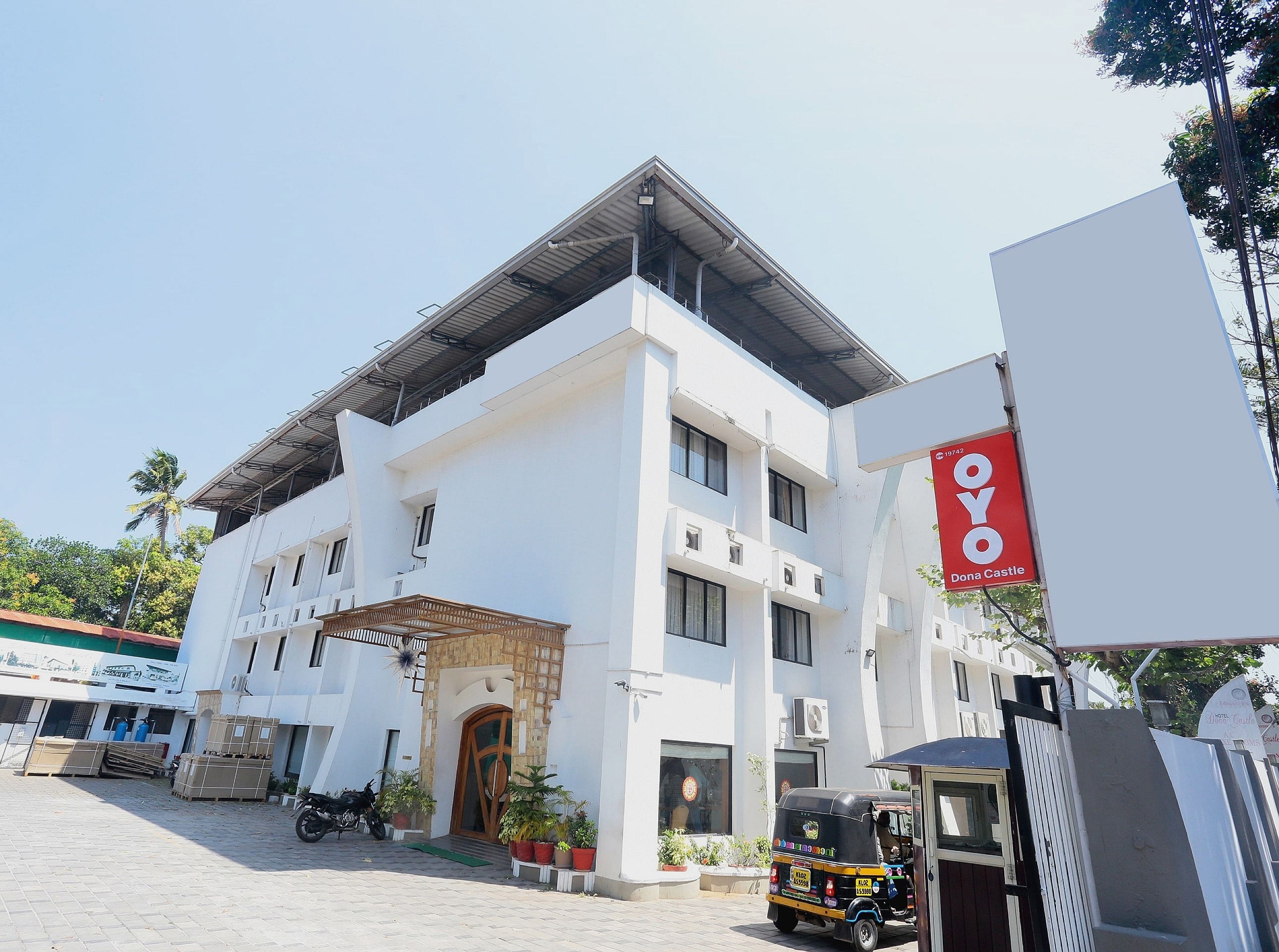 Un edificio de varios pisos con un letrero rojo llamativo de OYO Inn, una entrada con reja y un auto-rickshaw estacionado.