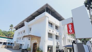 Un edificio de varios pisos con un letrero rojo llamativo de OYO Inn, una entrada con reja y un auto-rickshaw estacionado.