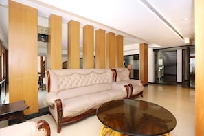A modern interior with a beige upholstered sofa, a glass coffee table, and wooden paneling.