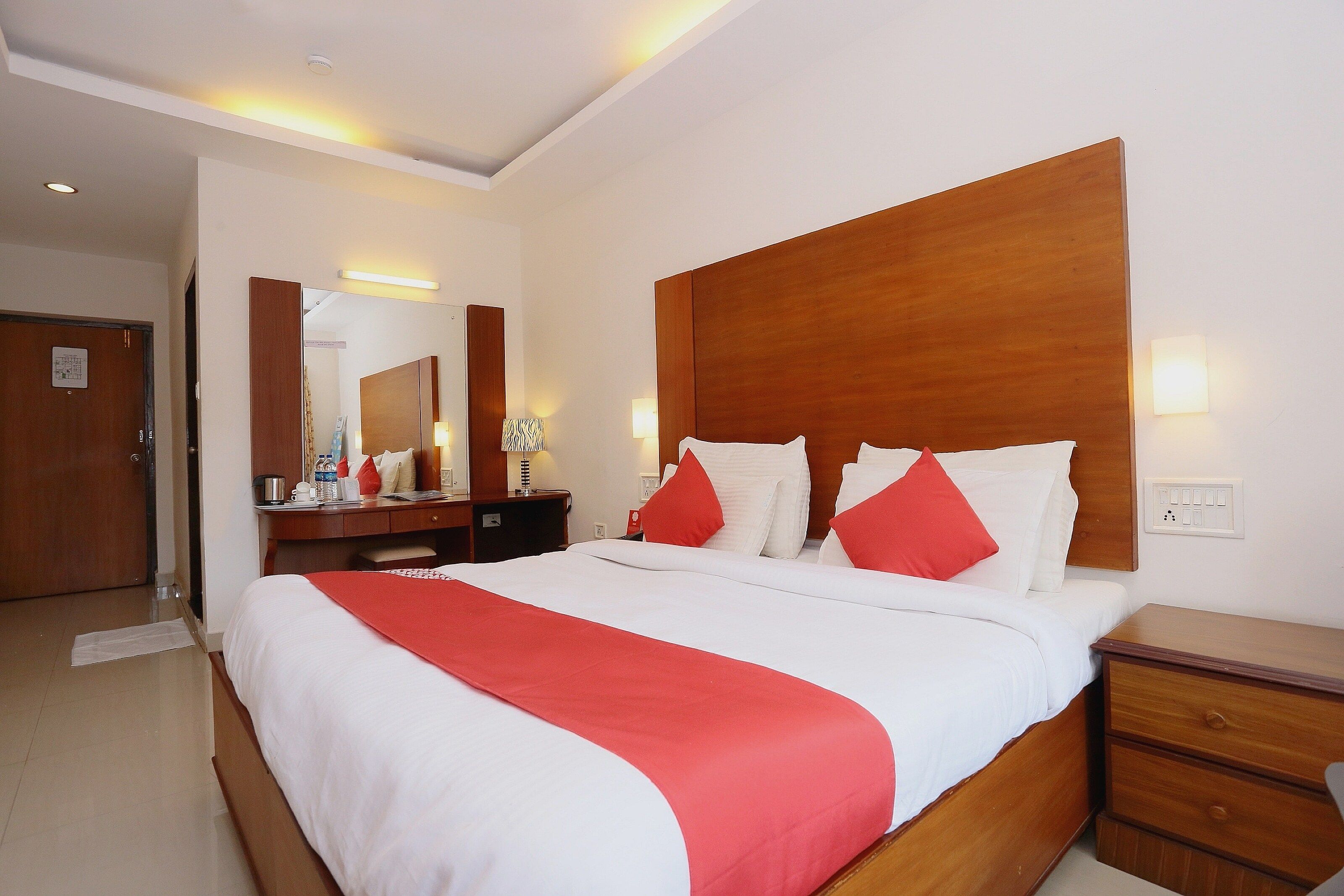 Een hotelkamer met een groot bed, een houten hoofdbord, een nachtkastje, een spiegel en een wandlamp.