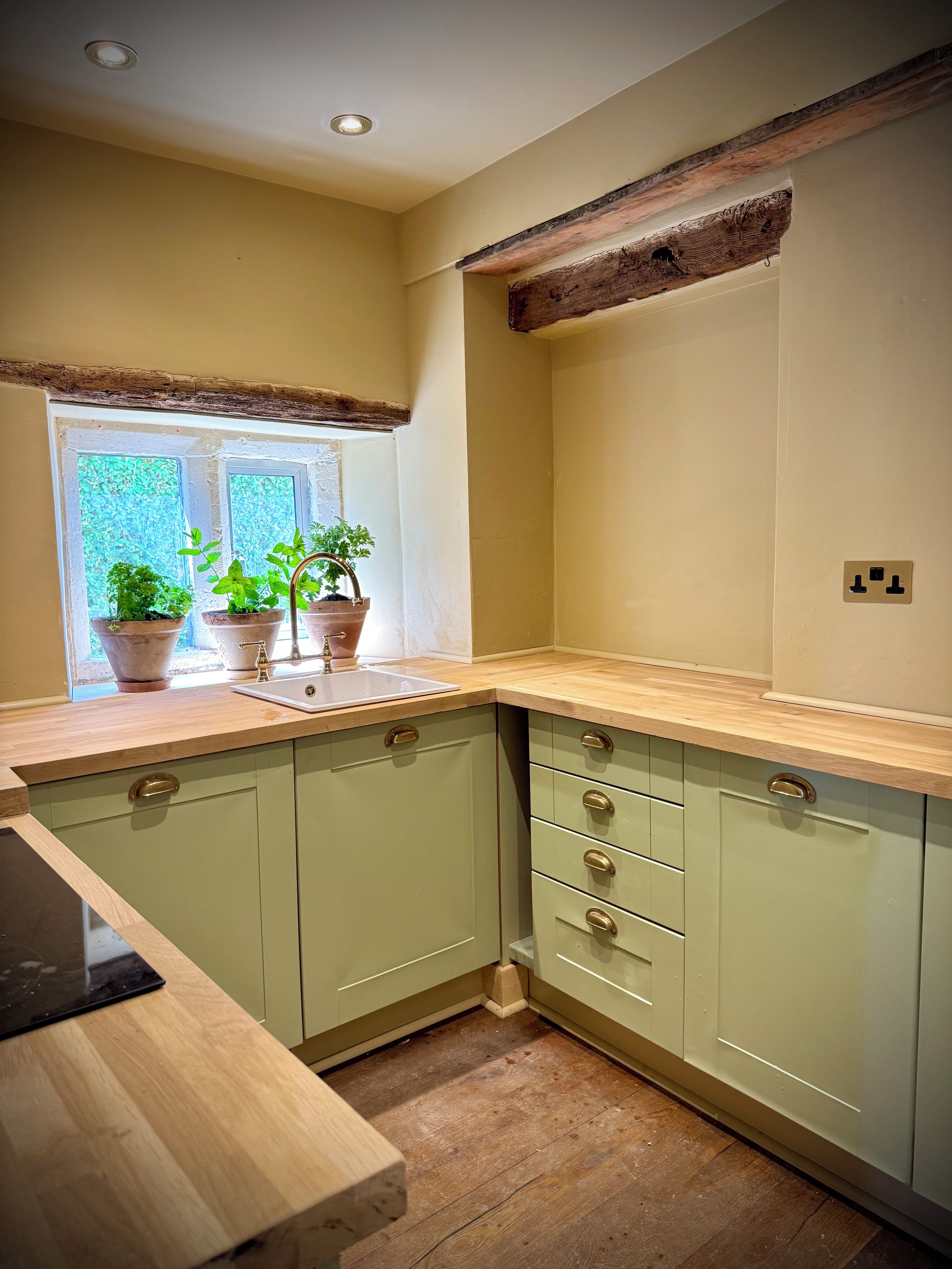 Een keuken met groene kastjes, een houten aanrechtblad en een raam met potplanten.