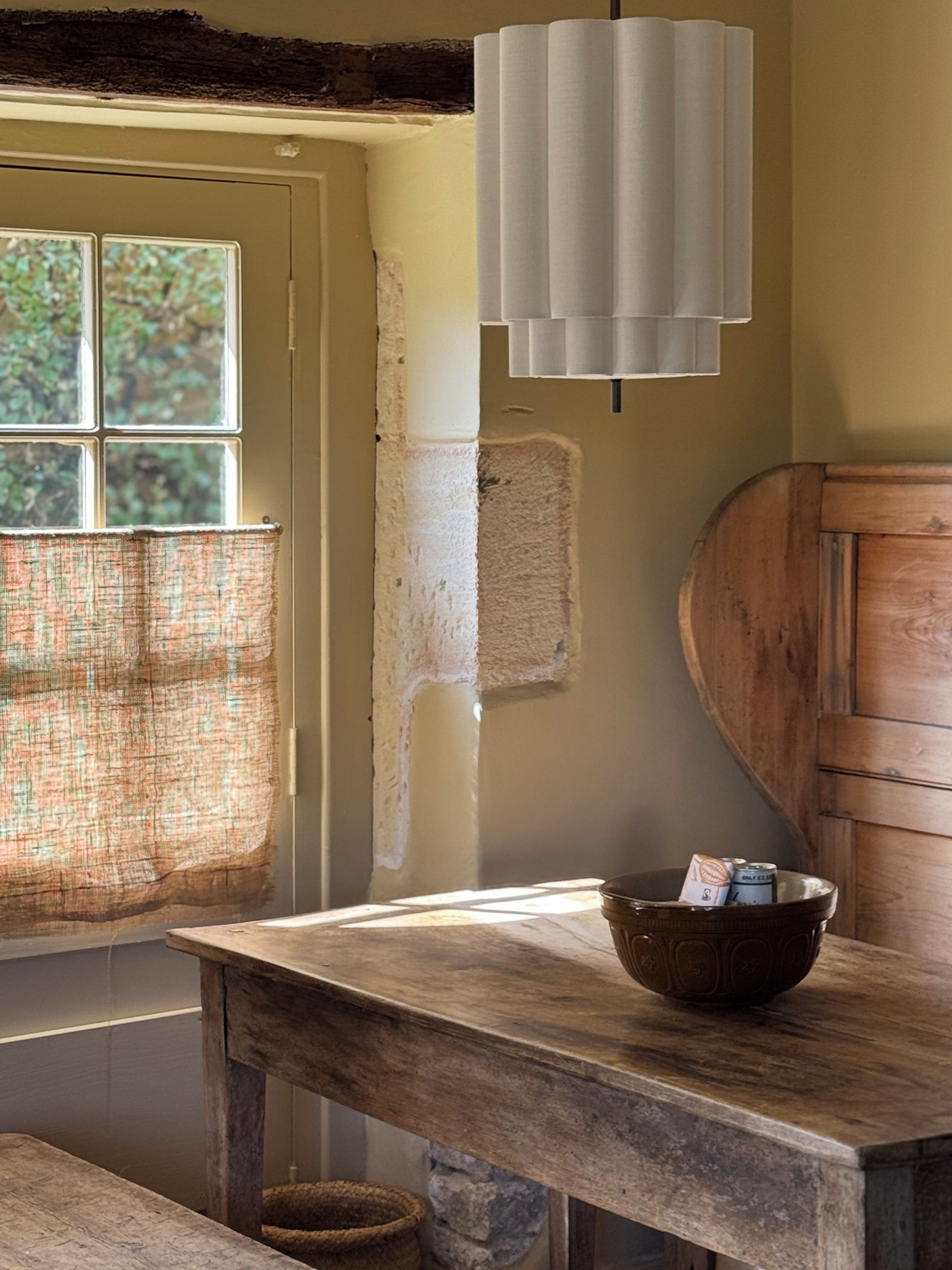 Un interior rústico con una mesa de madera, una lámpara colgante y una ventana con vistas a la vegetación.