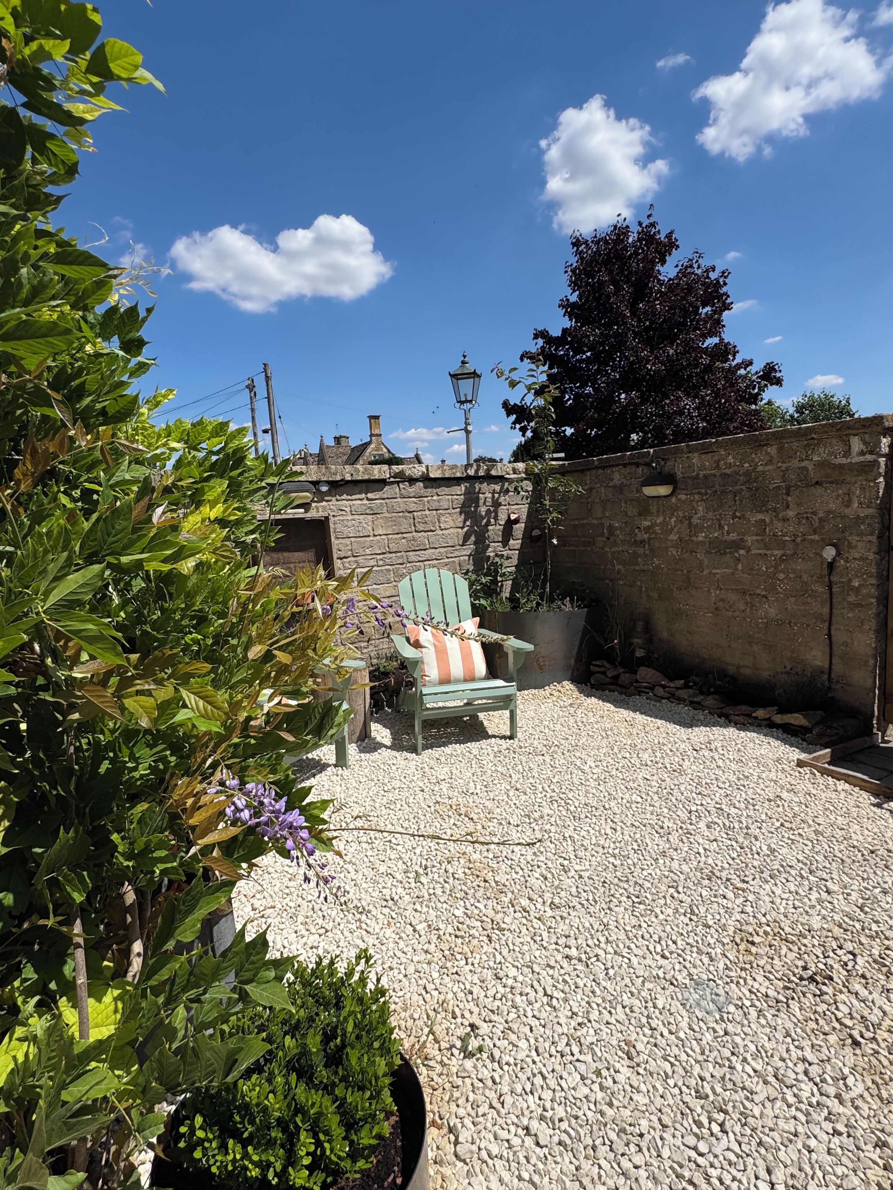 A garden patio with a chair, a lamp post, and a stone wall.