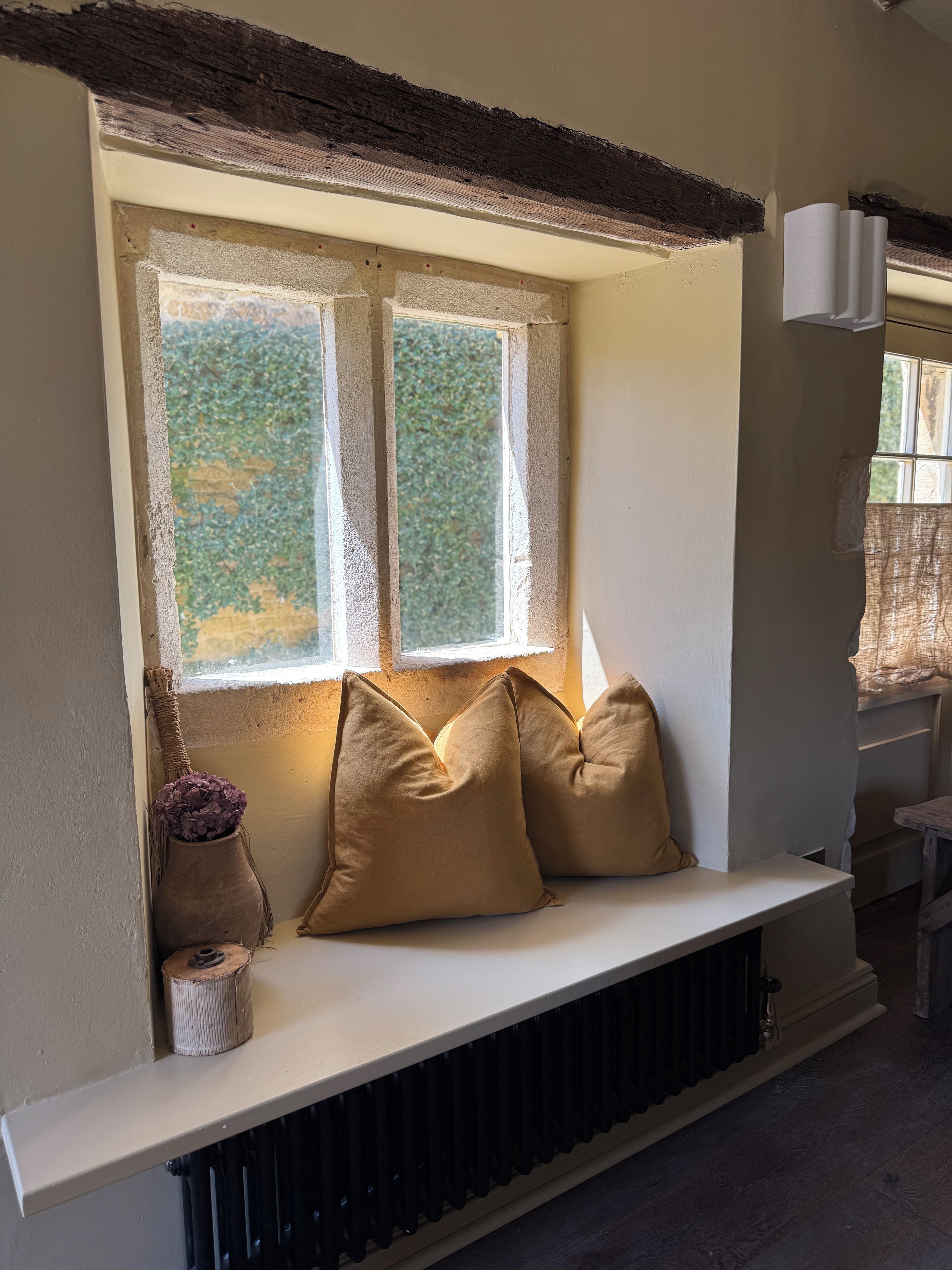 A room with a built-in bench under a window, a radiator below, and a small vase with flowers on the left.