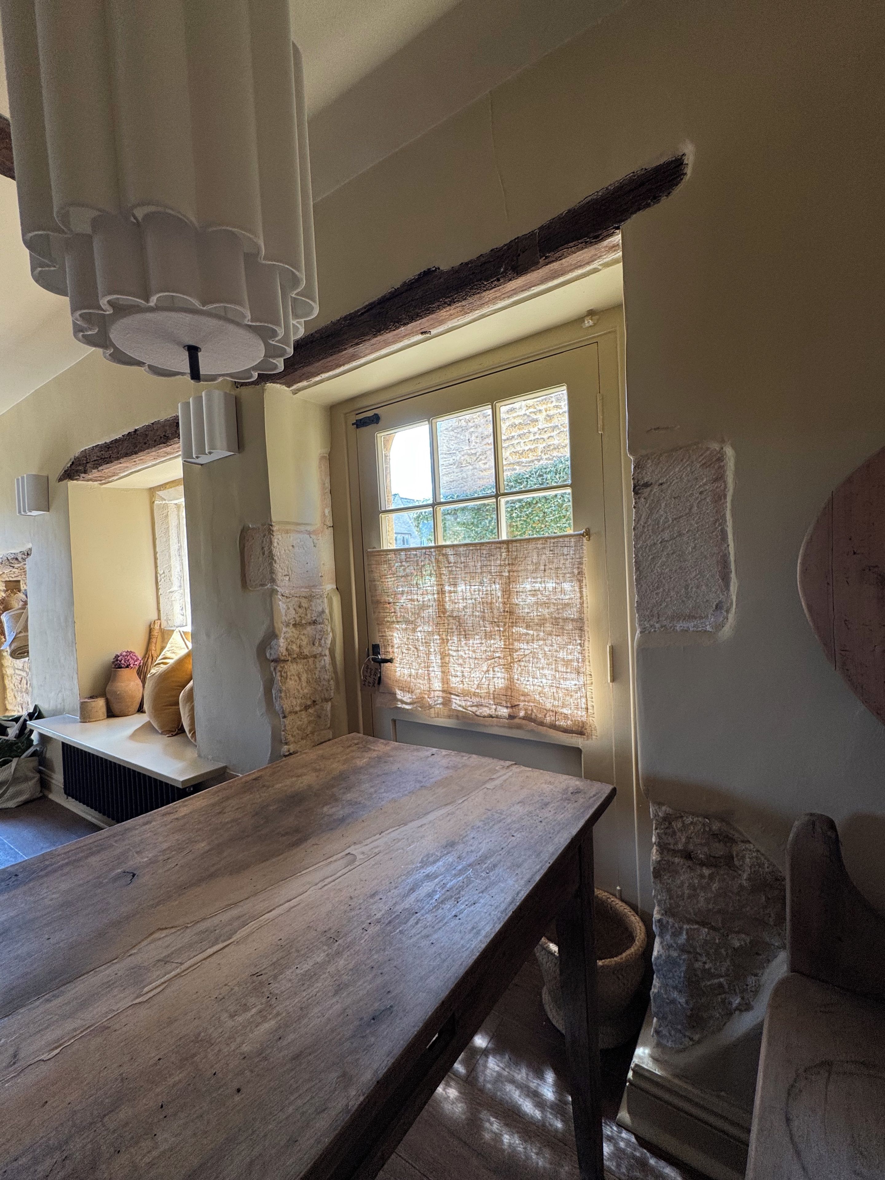 A room with a wooden table, stone walls, a window with a view, and a hanging light fixture.