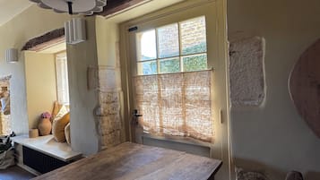 A room with a wooden table, stone walls, a window with a view, and a hanging light fixture.