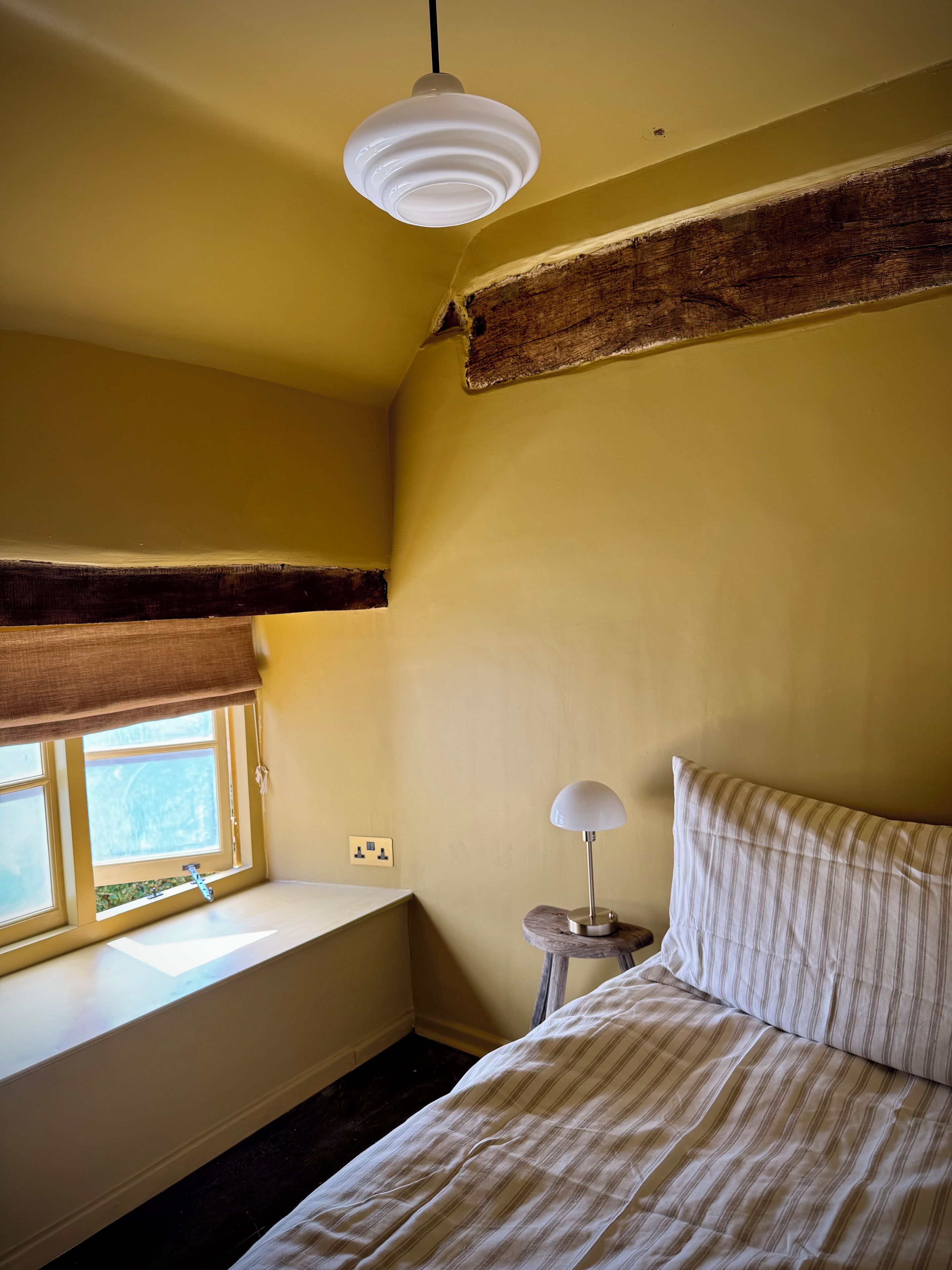 Een slaapkamer met een bed, een raam met uitzicht, een lamp en een plafondlamp.