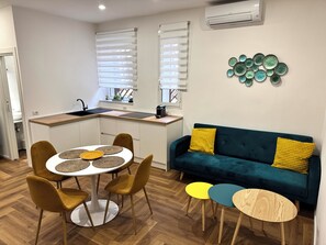 A compact living space with a kitchenette, a dining area with a round table and chairs, a sofa with cushions, and a decorative wall piece. - Vrbo Property (Roma)