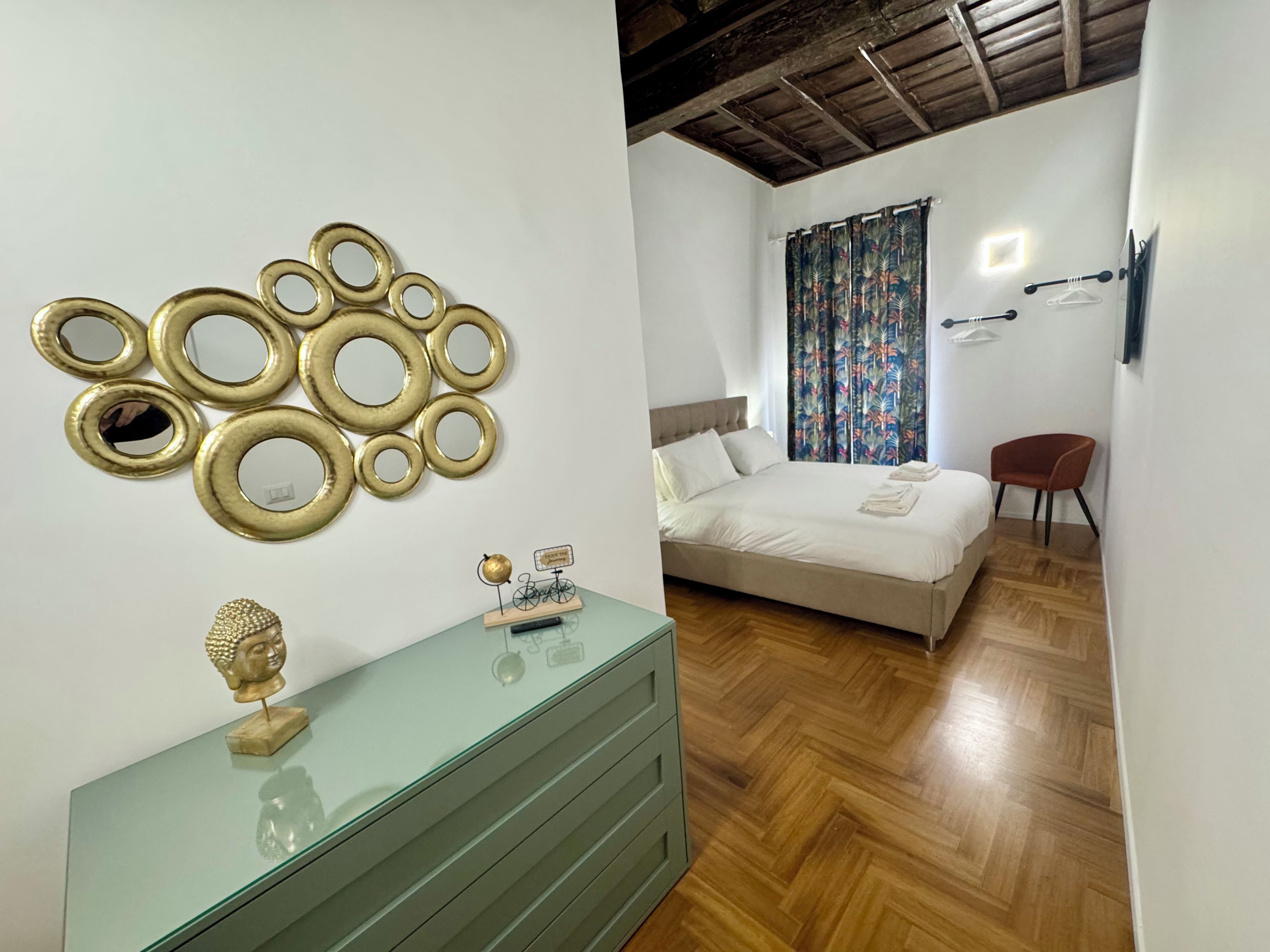 A bedroom with a bed, a green dresser, a wall-mounted mirror, and a decorative Buddha statue.