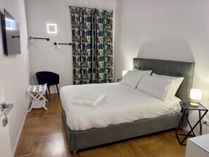 A neatly made bed with white linens, a grey upholstered headboard, and a bedside table with a lamp. - Vrbo Property (Roma)