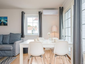 Ein modernes Wohnzimmer mit einem grauen Sofa, einem weißen Esstisch mit Stühlen, einer Lampe und einem Bild an der Wand.