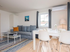 Ein modernes Wohnzimmer mit einer Couch, einem Esstisch mit Stühlen, einem Couchtisch und einer Lampe.