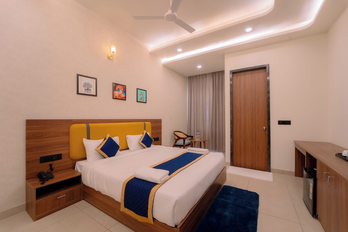 A hotel room with a bed, bedside table, nightstand, desk, chair, and a door.