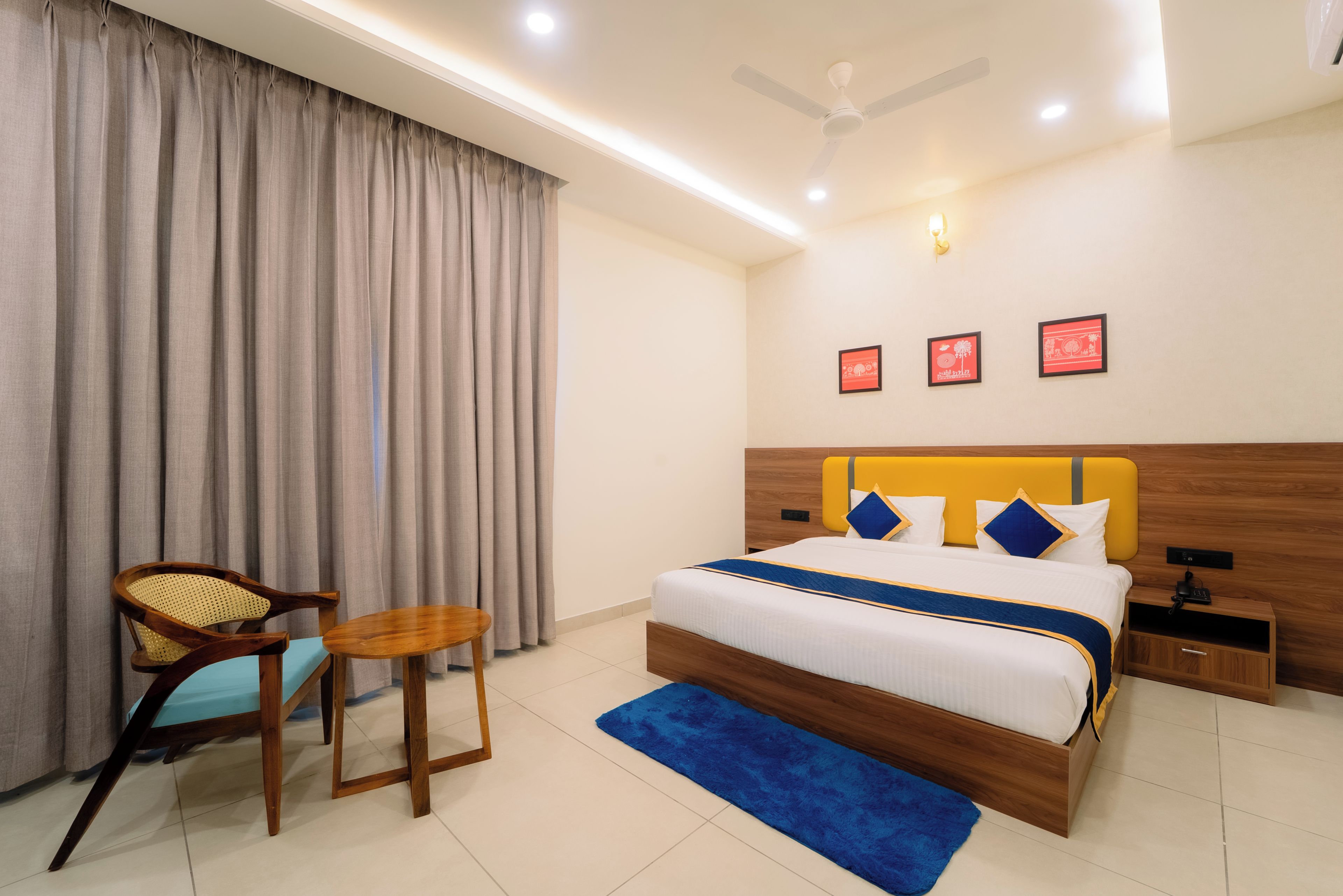 A hotel room with a bed, a chair, a small table, a ceiling fan, and wall-mounted lights.