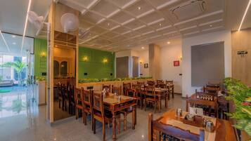A restaurant with wooden tables and chairs, a green accent wall, and a ceiling with recessed lighting.