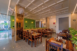 A restaurant with wooden tables and chairs, a green accent wall, and a ceiling with recessed lighting. - Shri Kalyan Hotel And Restaurant Khatu (Khatoo)