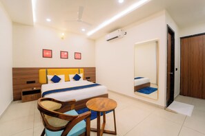 Habitación de hotel con cama, mesitas de noche, una silla, una mesa redonda, ventilador de techo, aire acondicionado instalado en la pared y un espejo.