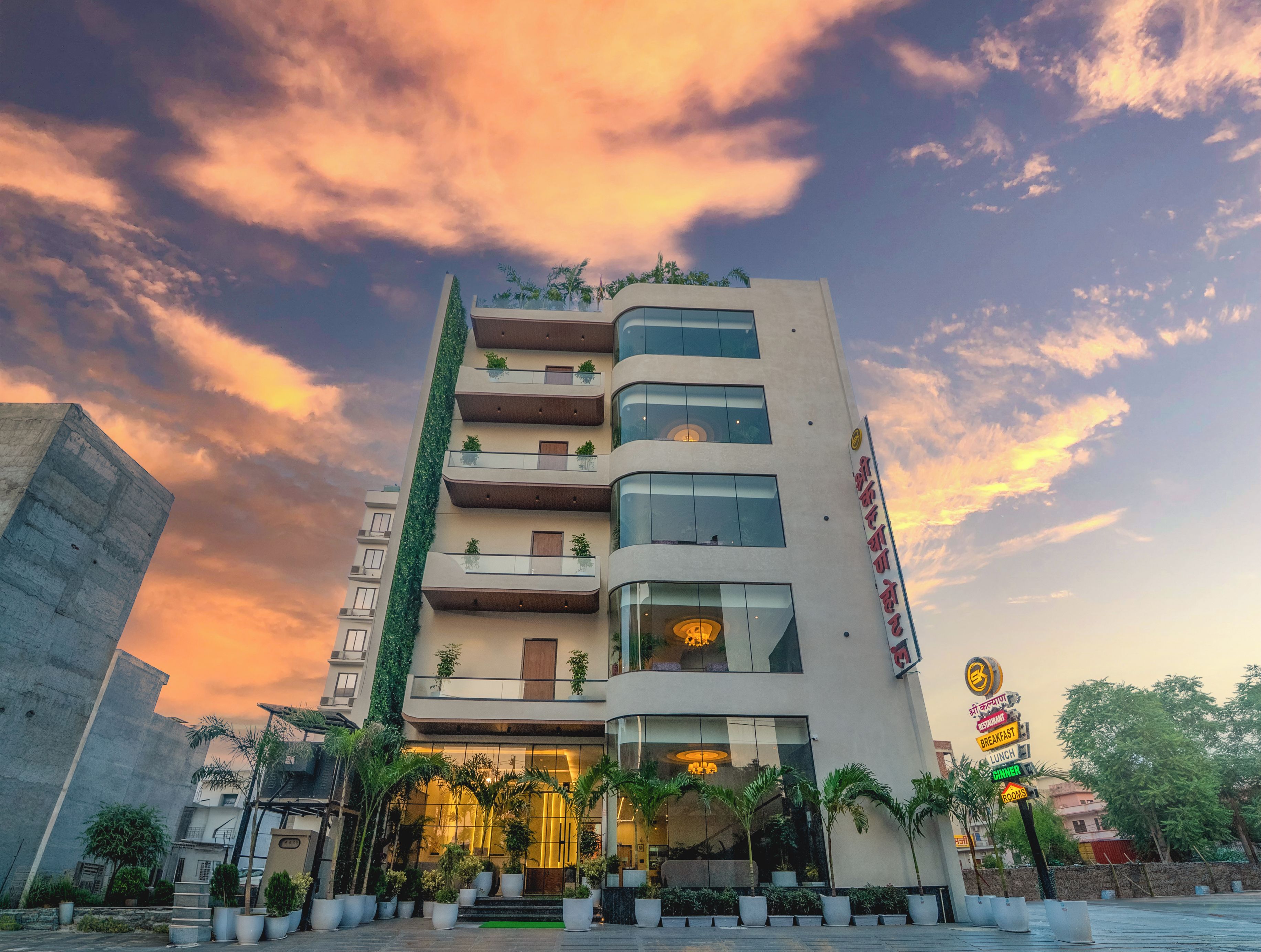 A multi-story hotel with a modern facade, balconies with plants, and a signboard indicating amenities.