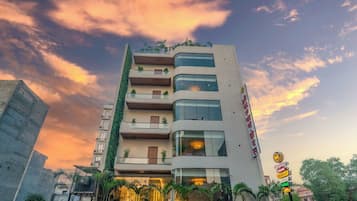 A multi-story hotel with a modern facade, balconies with plants, and a signboard indicating amenities.