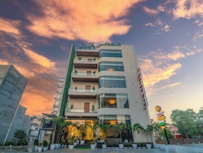 A multi-story hotel with a modern facade, balconies with plants, and a signboard indicating amenities. - Shri Kalyan Hotel And Restaurant Khatu (Khatoo)