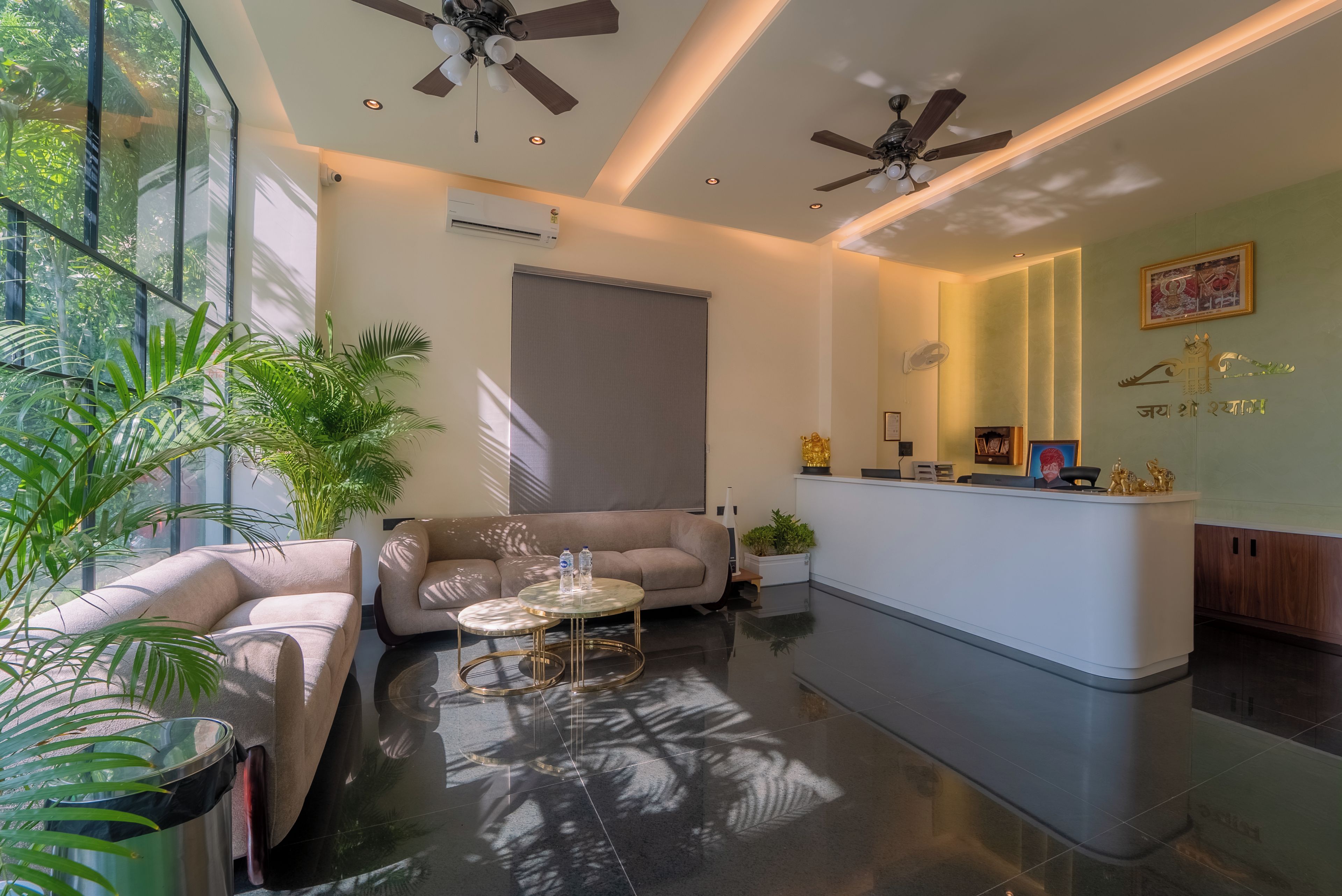 A modern hotel lobby with a reception desk, seating area, ceiling fans, and large windows.