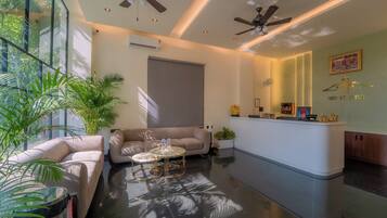 A modern hotel lobby with a reception desk, seating area, ceiling fans, and large windows.