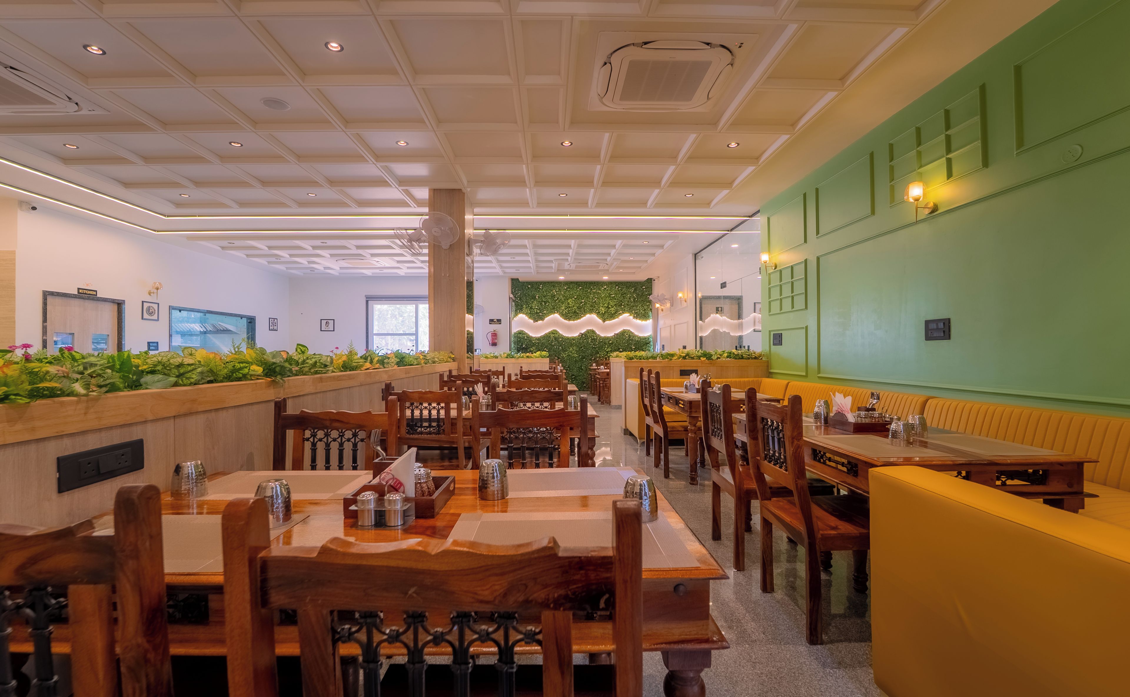 Un interior de restaurante con mesas y sillas de madera, una pared de acento verde y un techo con iluminación empotrada.