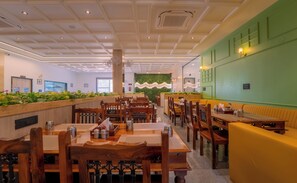 Un interior de restaurante con mesas y sillas de madera, una pared de acento verde y un techo con iluminación empotrada.