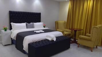 Una habitación de hotel con una cama grande, dos sillas, una mesita y una mesita de noche con lámpara.