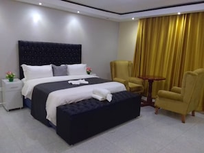 A hotel room with a large bed, two chairs, a small table, and a nightstand with a lamp. - Mazikana guest lodge, nestled high in the mountain, we offer best accommodation (Bindura)