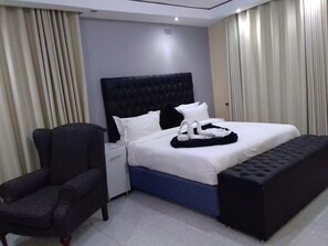 A hotel room with a bed, a chair, a nightstand, and a window with curtains.