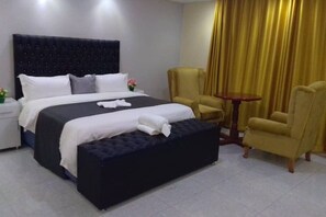 A hotel room with a large bed, a bedside table, a chair, and a small table.
