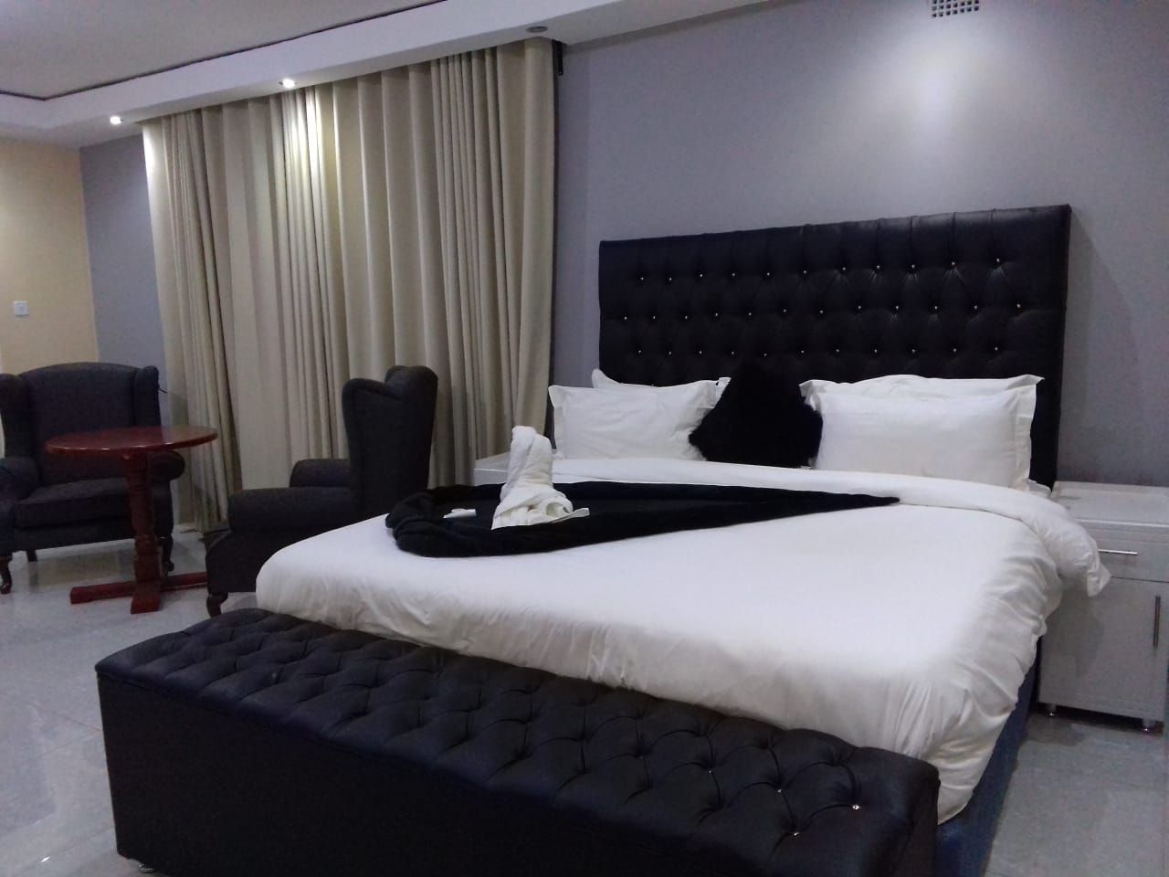 A hotel room with a large bed, a bedside table, a chair, and a window with curtains.