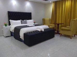 A hotel room with a large bed, a bedside table, a chair, and a small table. - Mazikana guest lodge, nestled high in the mountain, we offer best accommodation (Bindura)
